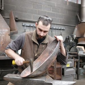 Editor Addison de Lisle hammering on a concave piece of metal atop an anvil.